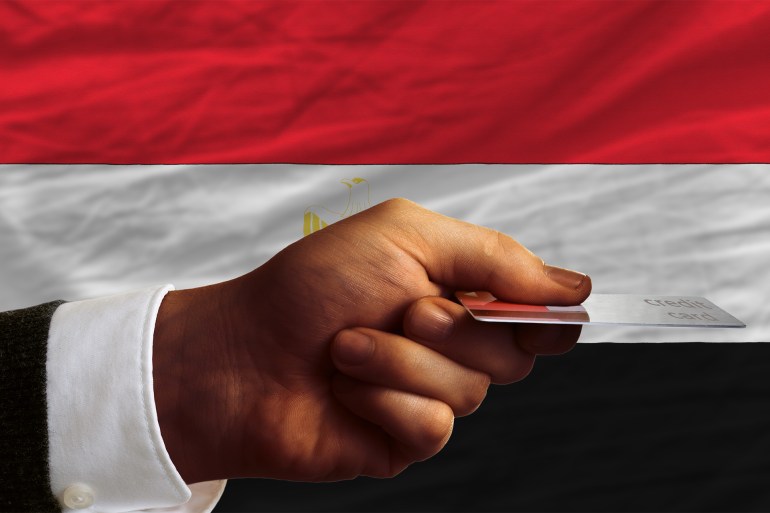 Buying with credit card in egypt - stock photo man stretching out credit card to buy goods in front of complete wavy national flag of egypt