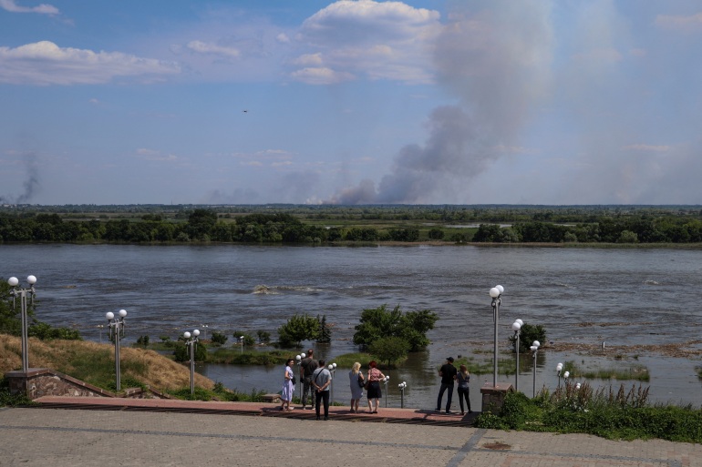 Local residents stand on an embankment of the Dnipro river which flooded after the Nova Kakhovka dam breached, in Kherson