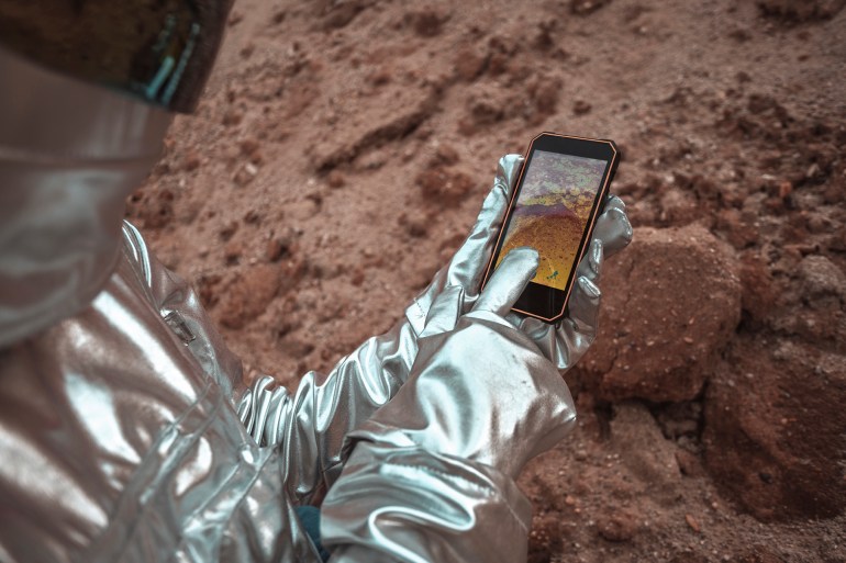 Spaceman examining new planet, using smartphone