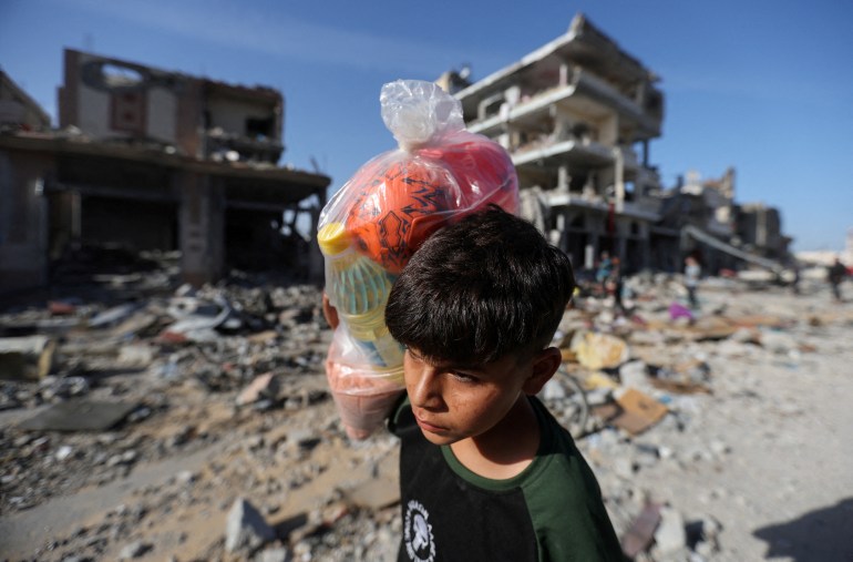 A displaced Palestinian boy carries a bag, as he returns to his home walking next to houses destroyed in an Israeli strike during the conflict, amid the temporary truce between Hamas and Israel, in Khan Younis in the southern Gaza Strip November 24, 2023. REUTERS/Ibraheem Abu Mustafa TPX IMAGES OF THE DAY