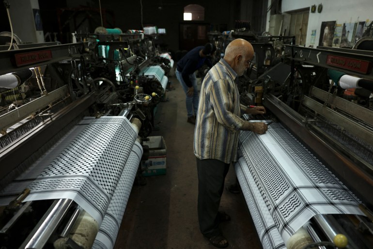 A worker stands over a loom at a textile factory producing the Palestinian Keffiyeh scarf in the occupied West Bank city of Hebron on November 20, 2023. (Photo by HAZEM BADER / AFP)