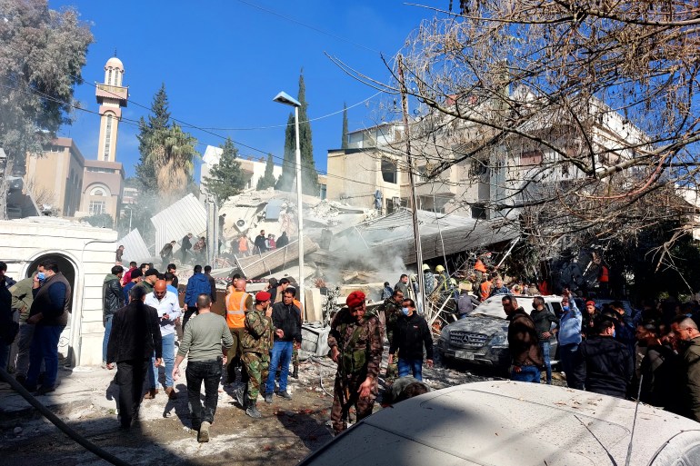 People and security forces gather in front of a building destroyed in a reported Israeli strike in Damascus on January 20, 2024. - An Israeli strike on Damascus killed five people in a building where "Iran-aligned leaders" were meeting on January 20, a war monitor said, as regional tensions soar over the Israel-Hamas war. (Photo by Louai Beshara / AFP)