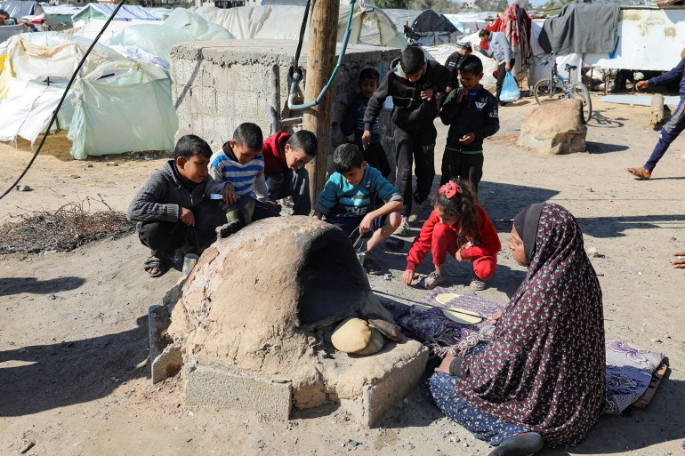 A Palestinian woman bakes bread as children sit next to her, while Gaza residents face crisis levels of hunger and soaring malnutrition, in Khan Younis in the southern Gaza Strip January 24, 2024. REUTERS/Arafat Barbakh