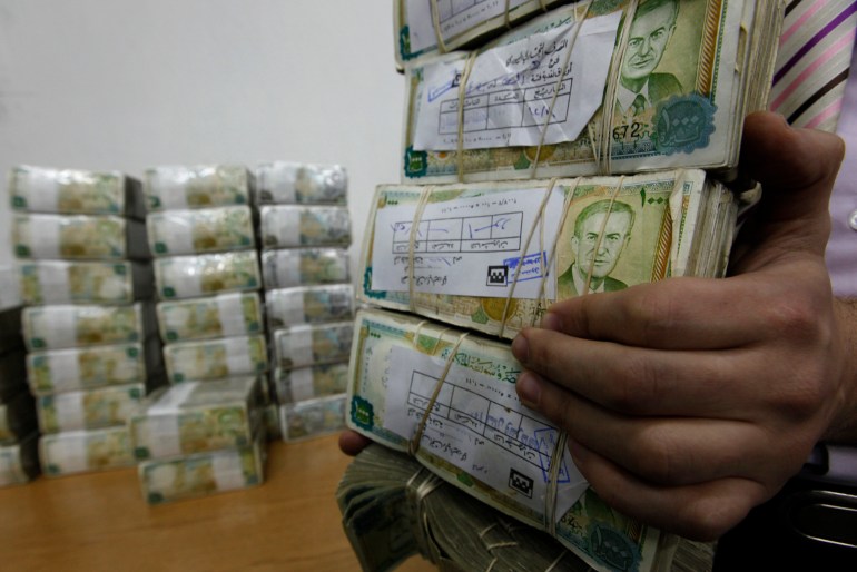 FILE - In this January 13, 2010 file photo, a Syrian employee, holds packets of Syrian currency in the Central Syrian Bank in, Damascus, Syria. With Syria's currency hitting record lows, a nationwide symbolic campaign has been launched by merchants, barbers, supermarkets and even gyms to support the Syrian pound. (AP Photo/Hussein Malla, File)