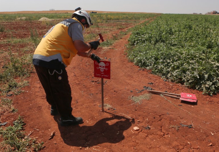 A member of the Syrian civil defence known as the White Helmets, fixes a sign cautioning about the presence of unexploded weapons in a field, on the outskirts of al-Jinah village in Syria's northern Aleppo province, on June 23, 2022. The shelling and airstrikes responsible for a large part of the Syrian war's half million deaths have decreased in recent years. But explosive remnants laid by all sides in the 11-year-old conflict are causing more deaths in Syria than anywhere else in the world, according to the United Nations. (Photo by Aaref WATAD / AFP)