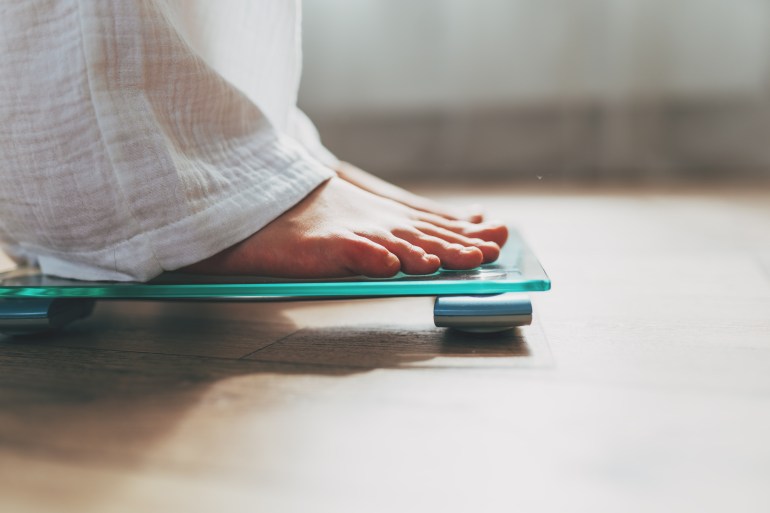 Female feet standing on electronic scales for weight control on wooden background. The concept of slimming and weight loss