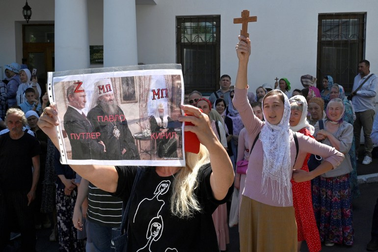 A woman holds a placard depicting Metropolitan Pavlo, the director of the Kyiv-Pechersk Lavra, staying next to Russian President Vladimir Putin as faithfuls of the Ukrainian Orthodox Church, accused of maintaining links with Russia, pray outside the historic monastery Kyiv-Pechersk Lavra to prevent tresspassing of the Ministry of Culture commission in Kyiv on July 4, 2023 (Photo by SERGEI CHUZAVKOV / AFP)