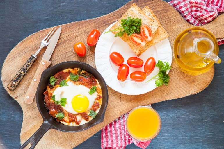 Pan of fried eggs and cherry-tomatoes with bread on dark table surface, top view, copy space, selective focus