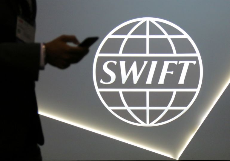 A man using a mobile phone passes the logo of global secure financial messaging services cooperative SWIFT at the SIBOS banking and financial conference in Toronto, Ontario, Canada October 19, 2017. REUTERS/Chris Helgren