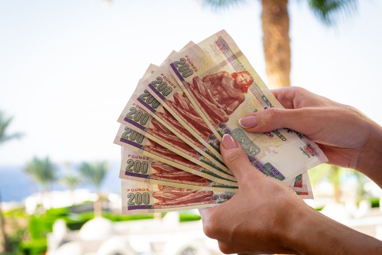 Young woman holding several Egyptian Pound banknotes on summer blurred background.